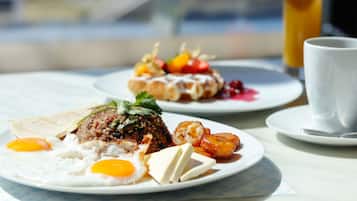 A breakfast setting with plates of food, including eggs, rice, and fruit, and a glass of orange juice.