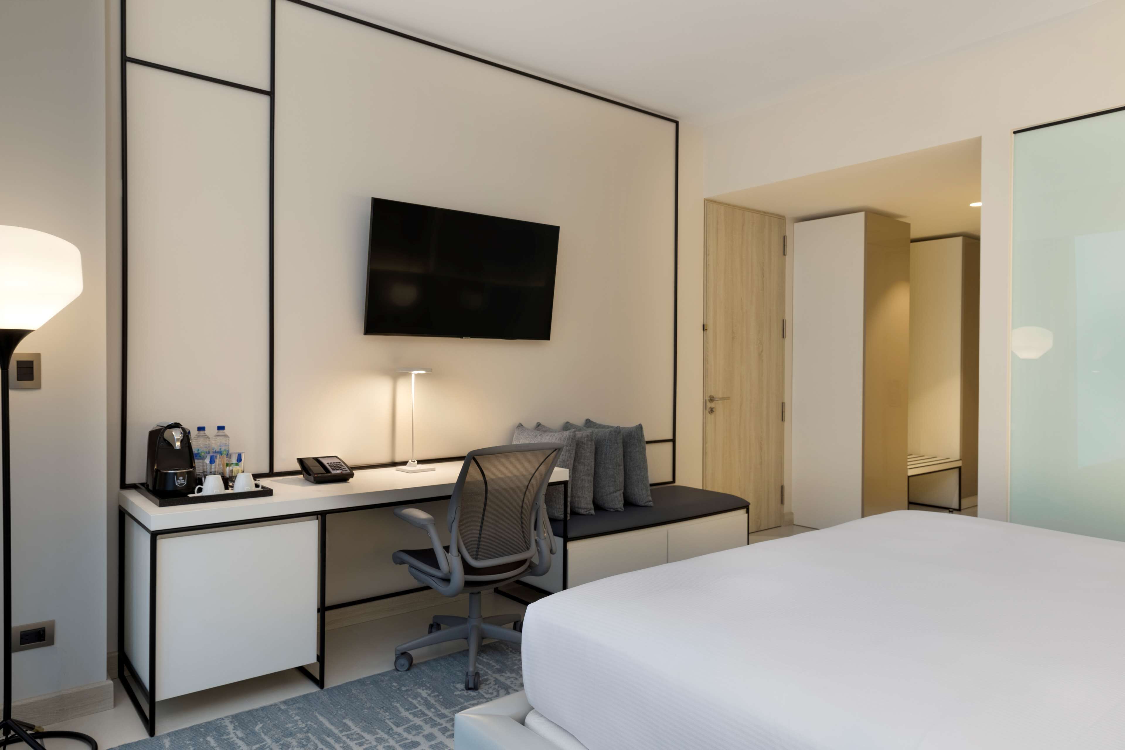 Habitación de hotel con cama, escritorio con silla, televisor de pantalla plana, cafetera y teléfono.