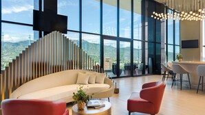 A modern interior with a large window, a sofa, red chairs, and a bar area. - Hilton San Jose La Sabana (San José)