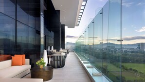 A modern balcony with a glass railing, offering a view of a cityscape and green park. - Hilton San Jose La Sabana (San José)