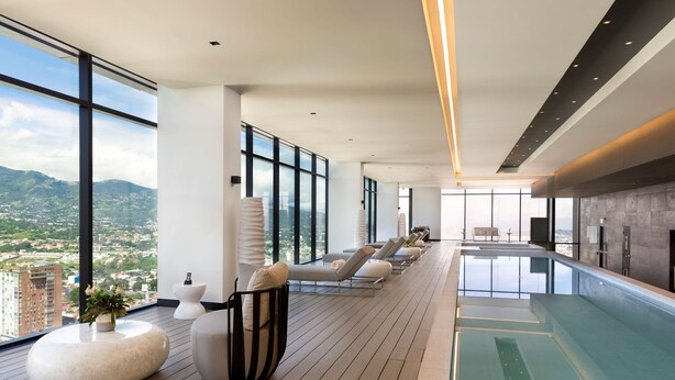 A modern rooftop lounge with a pool, large windows, and a view of the city. - Hilton San Jose La Sabana (San José)