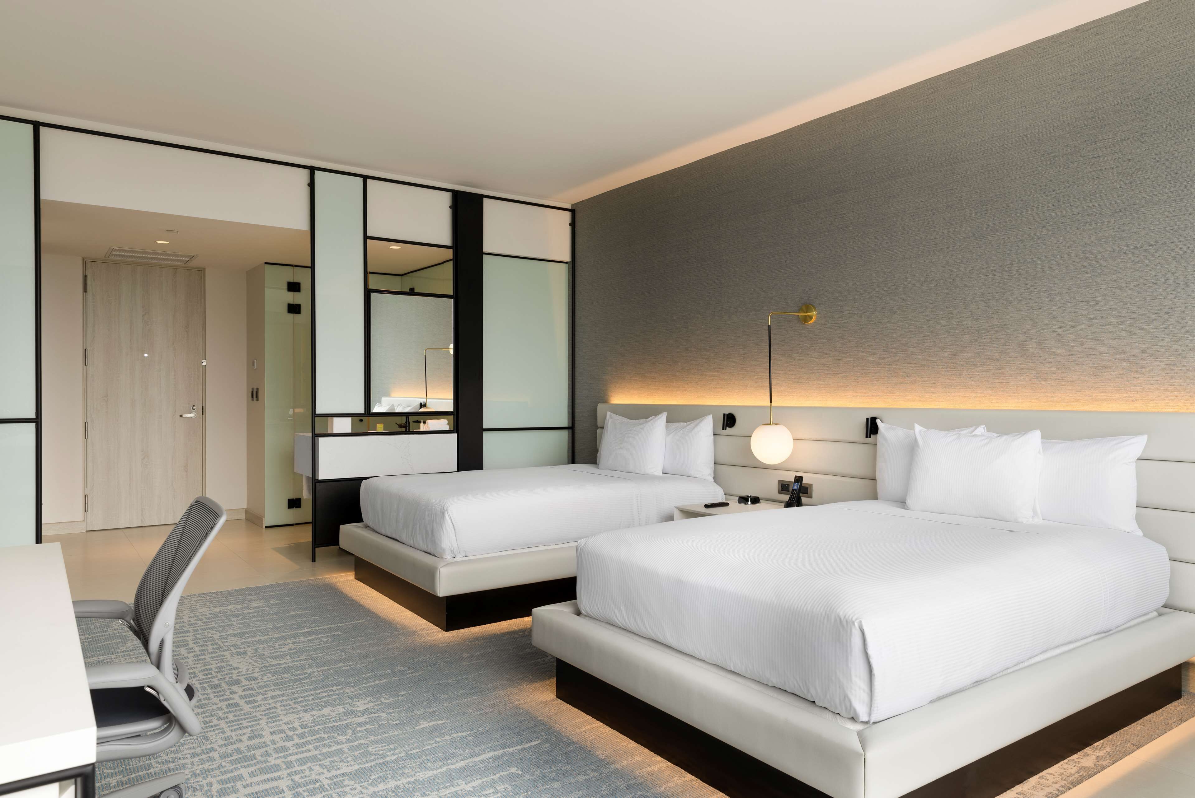 A modern hotel room with two beds, a desk, and a large mirror.