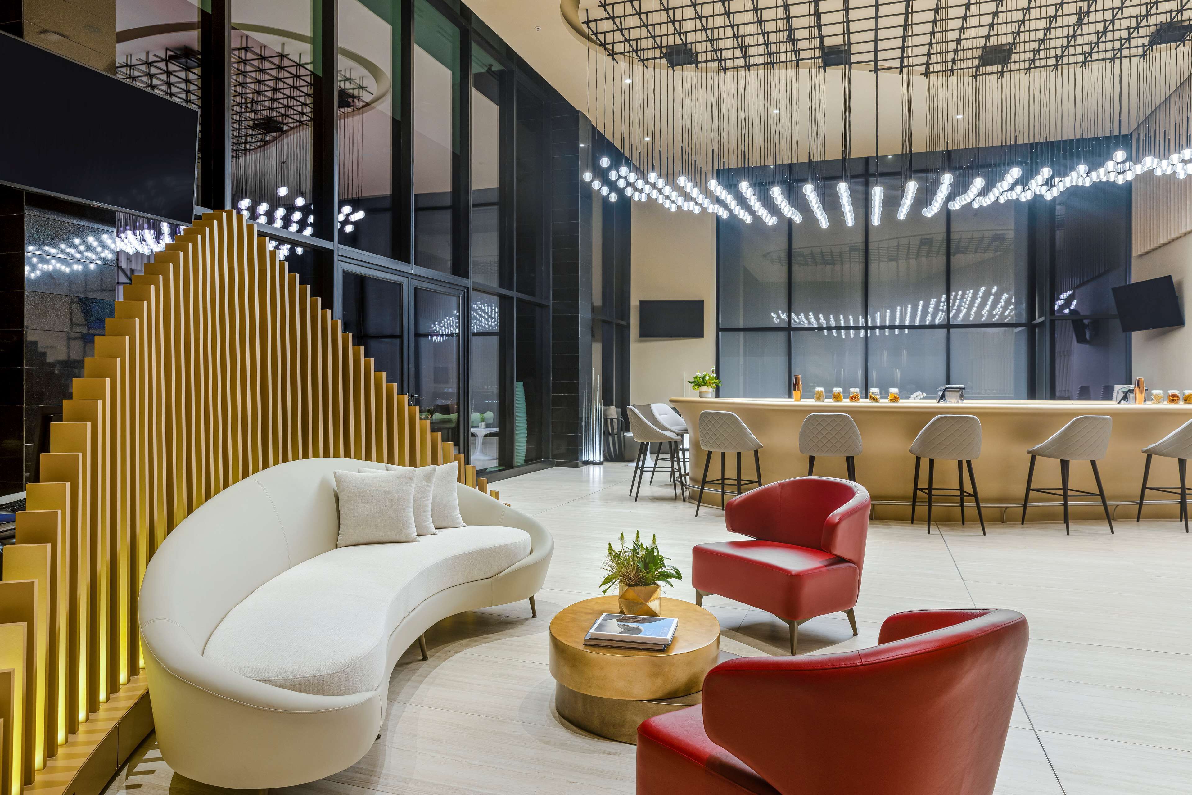 Ein modernes Interieur mit einem gebogenen weißen Sofa, roten Sesseln, einer Holztreppe und einer Bar mit Hockern.
