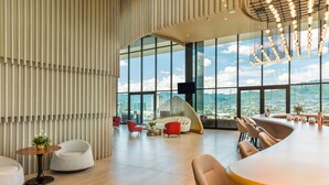 A spacious, modern lounge with a high ceiling, large windows offering a cityscape view, and contemporary furniture. - Hilton San Jose La Sabana (San José)