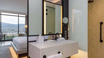 A modern hotel bathroom with a large mirror, a white sink, and a shower area.