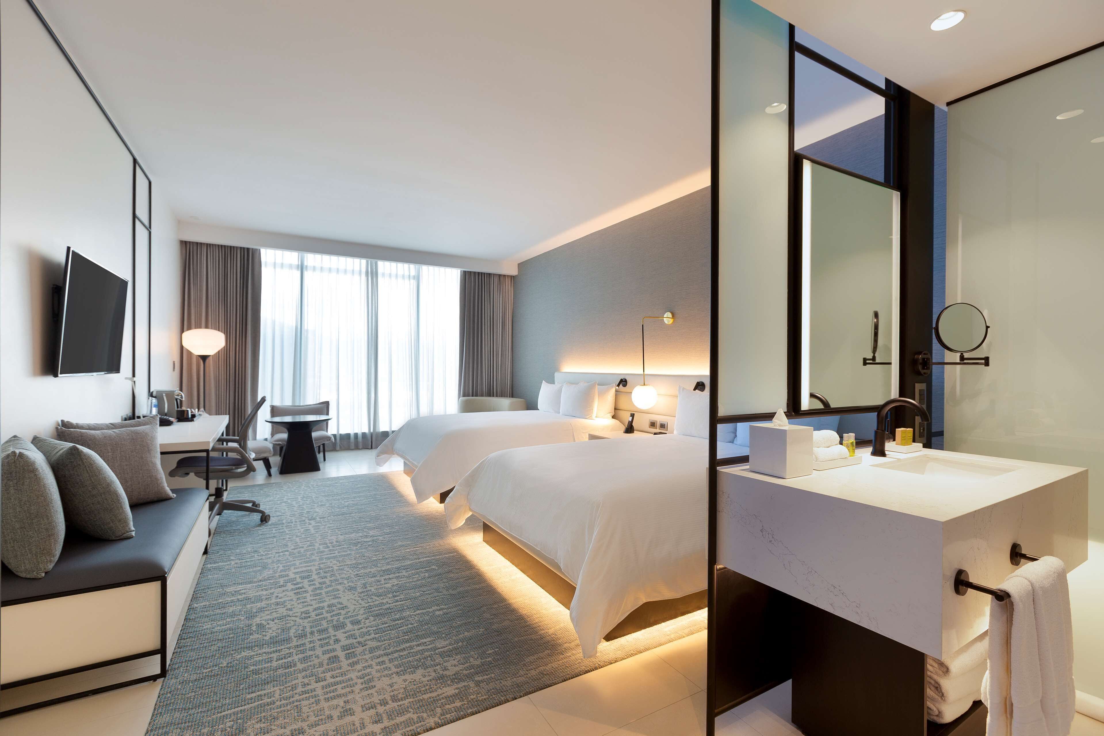 Hotelkamer met een bed, bureau, stoel, bank, grote spiegel en een badkamer met wastafel en handdoekhouder.