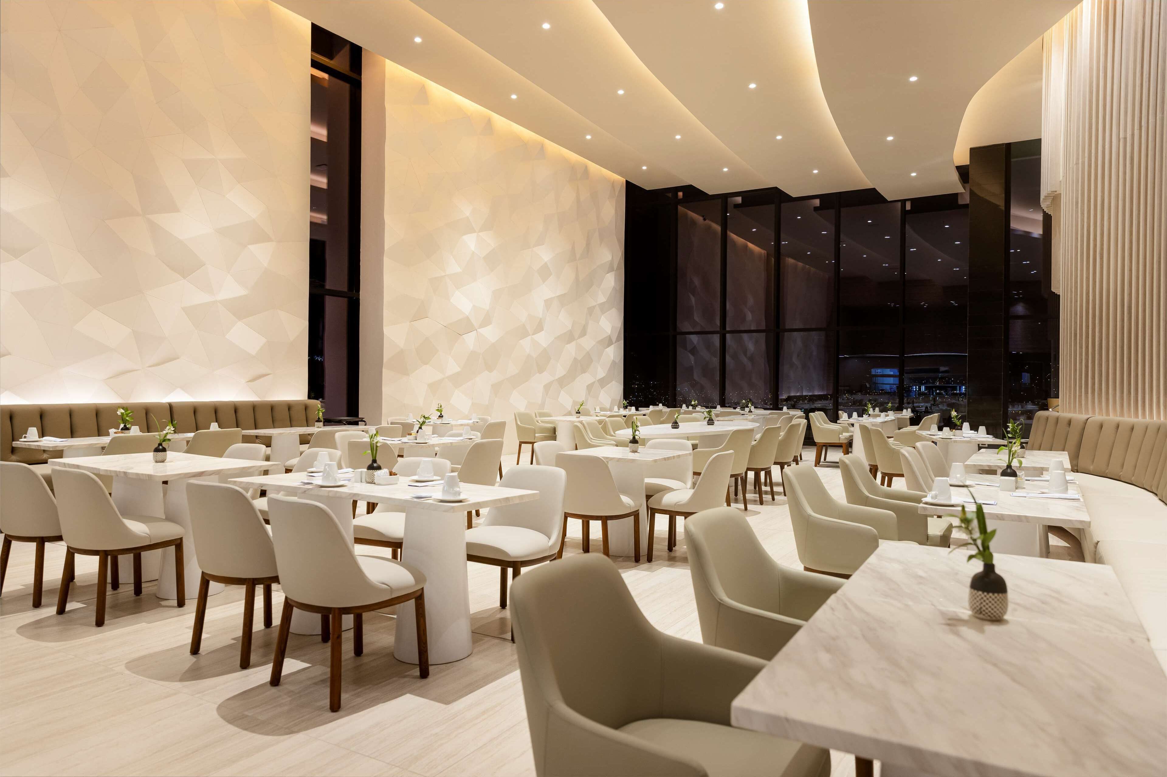 A modern restaurant with a geometric wall design, multiple dining tables, and chairs.