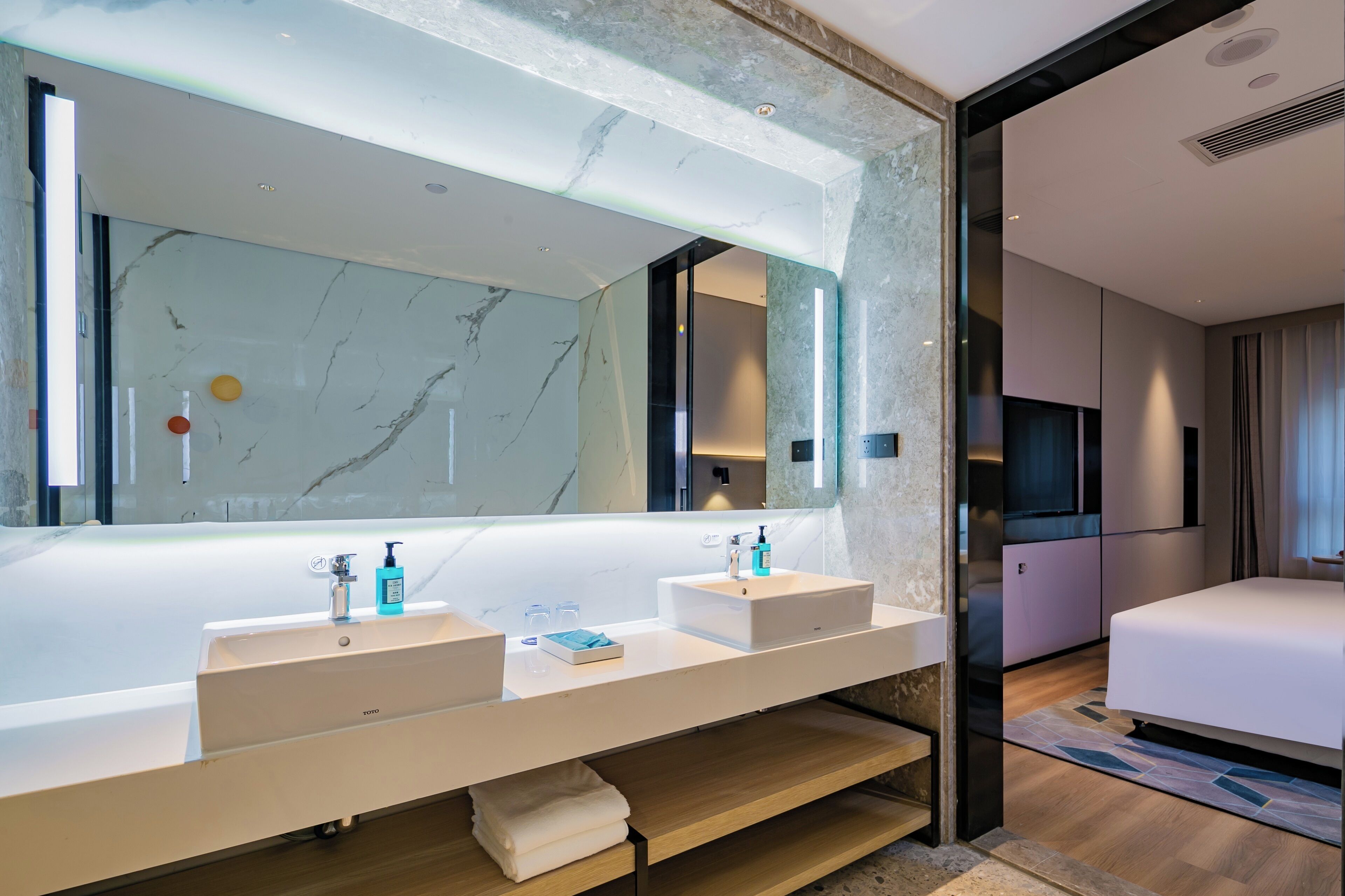 A modern bathroom with a large mirror, two sinks, and a vanity with storage.
