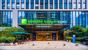 Et Holiday Inn Express hotel med en moderne glasfacade, et udendørs siddeområde og en godt oplyst indgang.