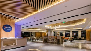 En moderne hotellobby med reception, siddeområde og et stort spejl der afspejler rummet.