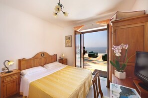 A bedroom with a bed, bedside table, lamp, TV, and a view of the sea. - Villa Superba Summary (Massa Lubrense)