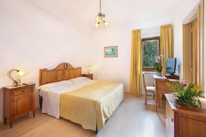 Un dormitorio con una cama de madera, mesitas de noche, un escritorio con silla, un televisor y una ventana con cortinas.