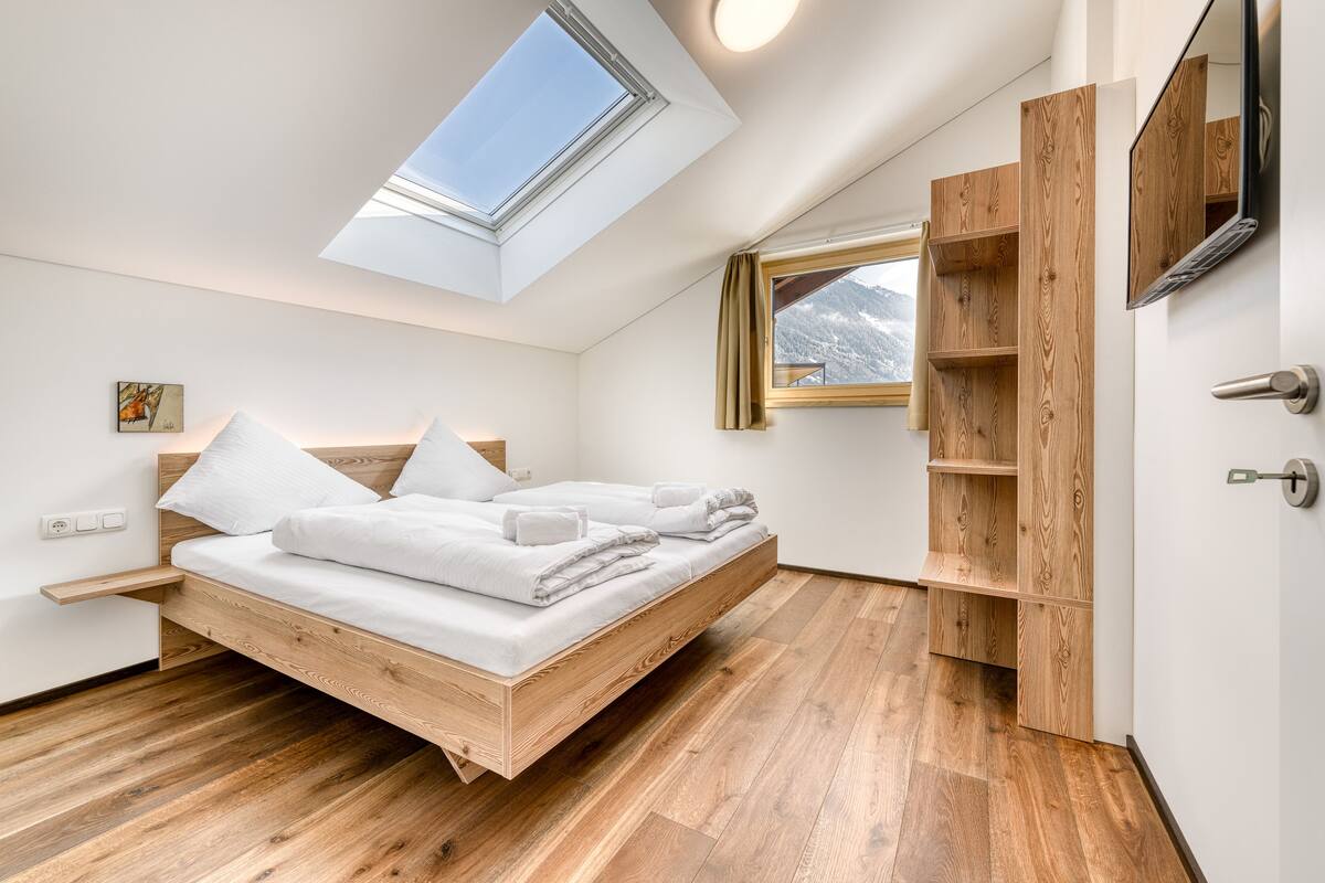 Camera da letto moderna con lucernario, struttura del letto in legno e scaffalature integrate in legno.