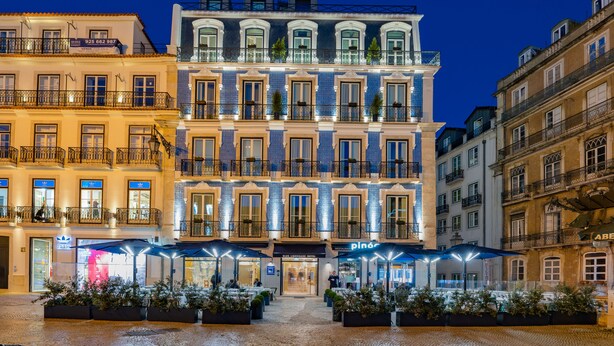 Un hotel con varios pisos, mobiliario exterior y una fachada bien iluminada.