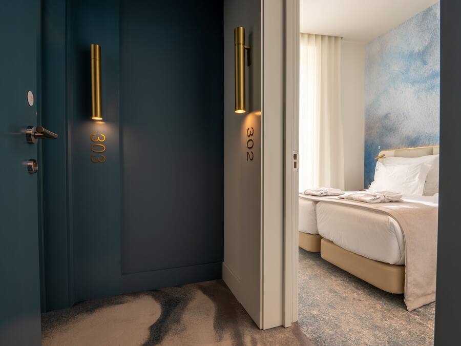 A modern hotel room with a blue accent wall, a bed with white linens, and a door with the number 302.