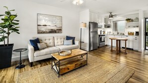A modern kitchen with white cabinets, a stainless steel refrigerator, and a dining area with a wooden table. - Kailua Village #701: Top Floor, Corner Penthouse Remodeled in Downtown Kona. (Kailua Kona)