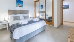 Una habitación de hotel moderna con una cama grande, mesitas de noche, un armario y un espejo.