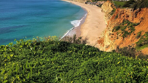 Un paisaje costero con playa, acantilados y un pueblo al fondo.