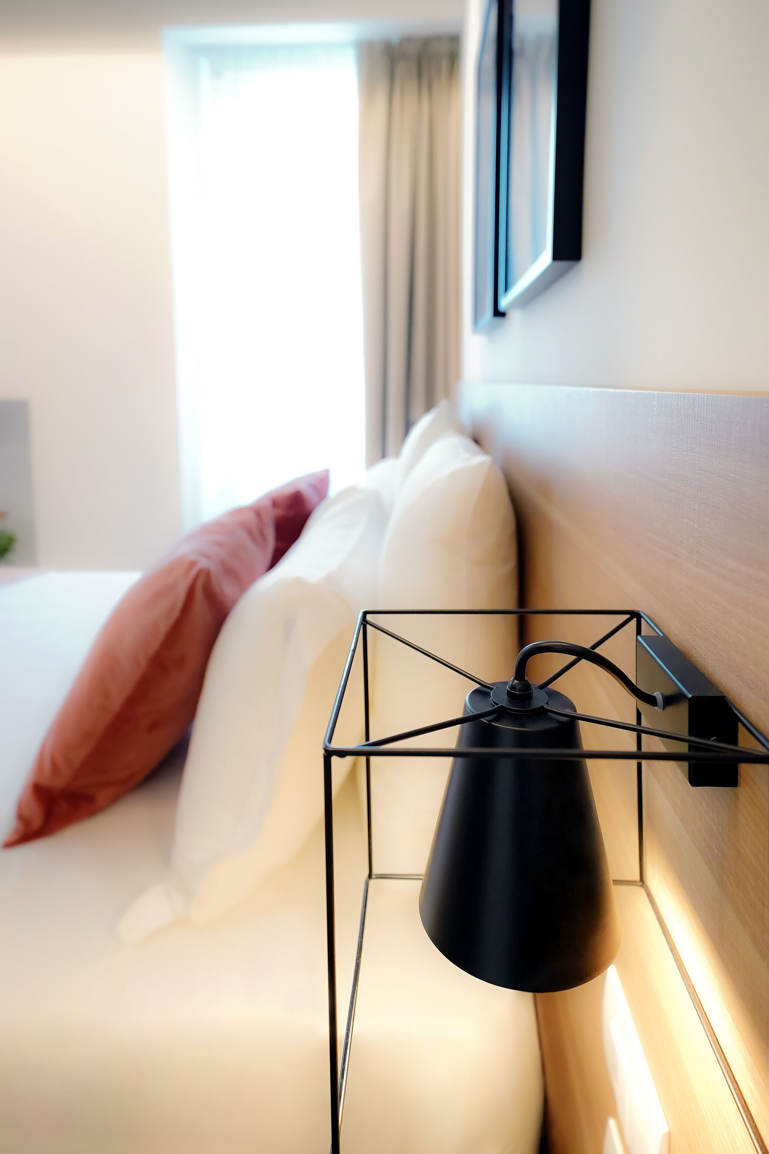 A neatly made bed with white and pink pillows, a black hanging lamp, and a wooden headboard.