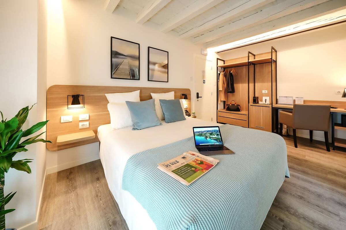A modern hotel room with a bed, a desk, and a wardrobe.