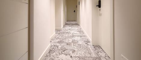 A long, narrow hotel corridor with a patterned carpet, white walls, and doors on both sides.