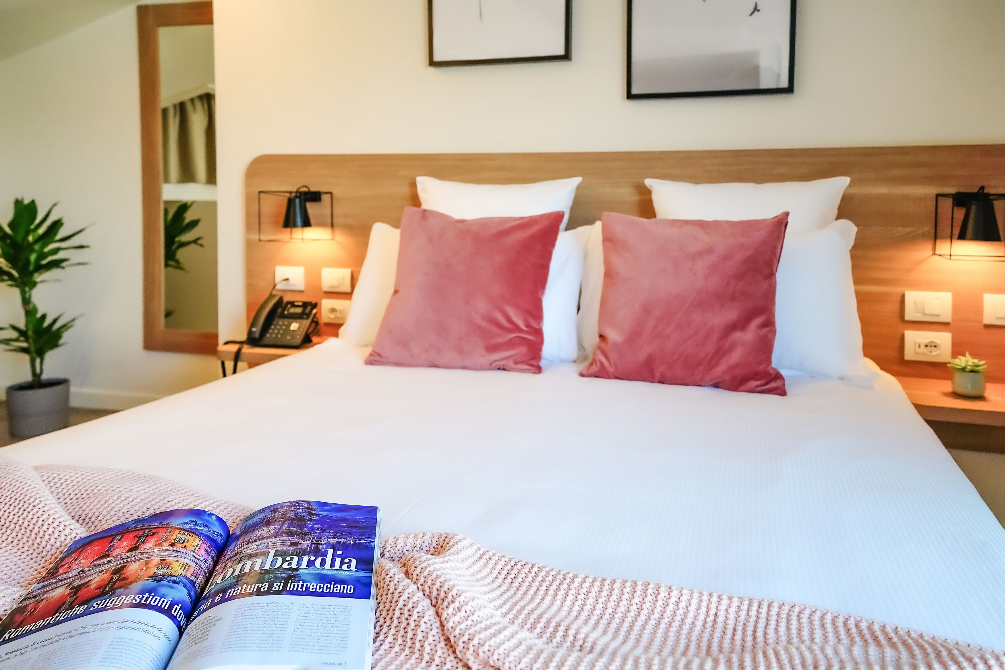 A hotel room with a neatly made bed, a bedside telephone, a lamp, and a magazine on the bed.