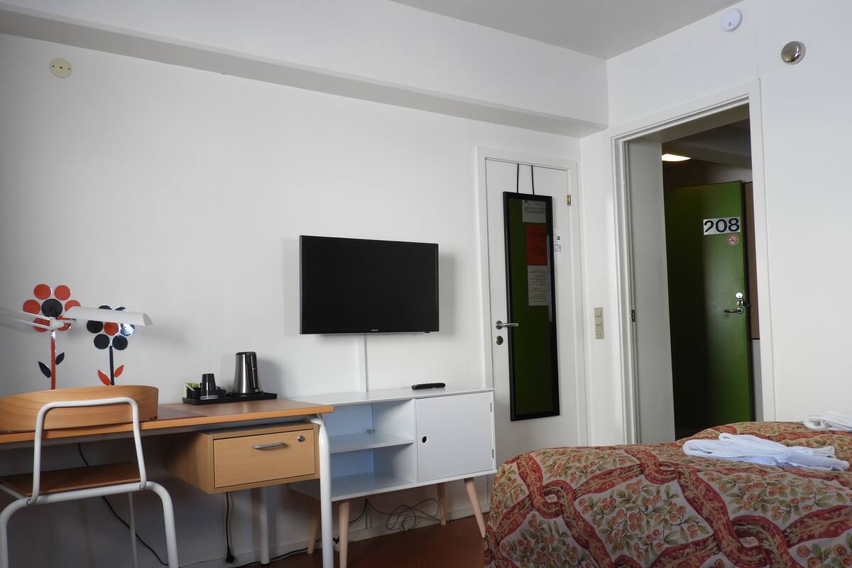 A hotel room with a desk, chair, bed, and a television.