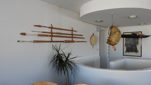 Un baño con una bañera blanca, un toallero de madera con diversos utensilios de aseo, una bolsa de cuero colgante y una obra de arte enmarcada.