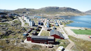 An aerial view of a coastal town with buildings, a road, and a lake. - Sulisartut Højskoliat (Qaqortoq)