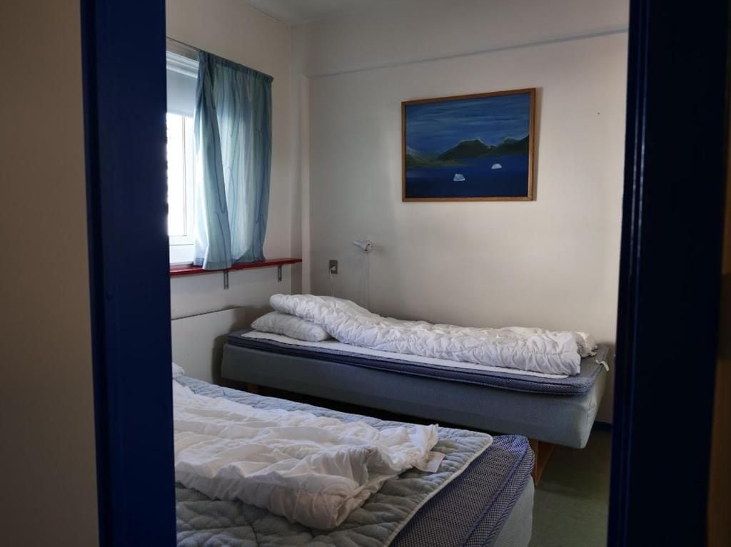 A room with two beds, a painting on the wall, and a window with curtains.