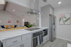A modern kitchen with a large island, stainless steel appliances, and a minimalist design. - Vibrant Spacious Home w/ Private Pool and Jacuzzi (Richardson)