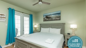 A clean, well-lit bedroom with a large bed, a ceiling fan, and a painting of a boat on the wall. - Cozy Studio Getaway with Pool, Hot Tub, Fishing Pond, & Easy Beach Access (Corpus Christi)