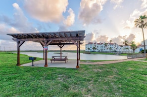 A wooden gazebo with benches, a mailbox, and a view of a body of water and buildings in the background. - Cozy Studio Getaway with Pool, Hot Tub, Fishing Pond, & Easy Beach Access (Corpus Christi)