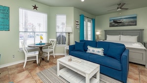 A living room with a blue sofa, white coffee table, and a dining area with a white table and chairs. - Cozy Studio Getaway with Pool, Hot Tub, Fishing Pond, & Easy Beach Access (Corpus Christi)