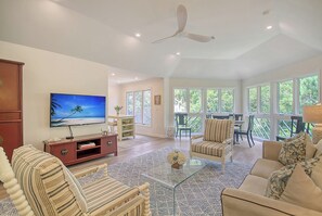 A spacious living room with a large TV, comfortable seating, and a ceiling fan.