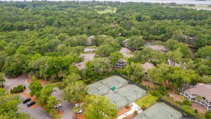 An aerial view of a residential area with a tennis court surrounded by lush greenery and houses.