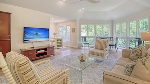 A spacious living room with a large TV, comfortable seating, and a ceiling fan.