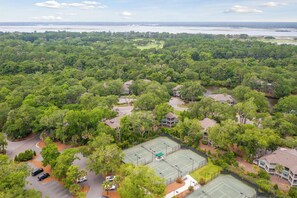 An aerial view of a residential area with a tennis court surrounded by lush greenery and houses.