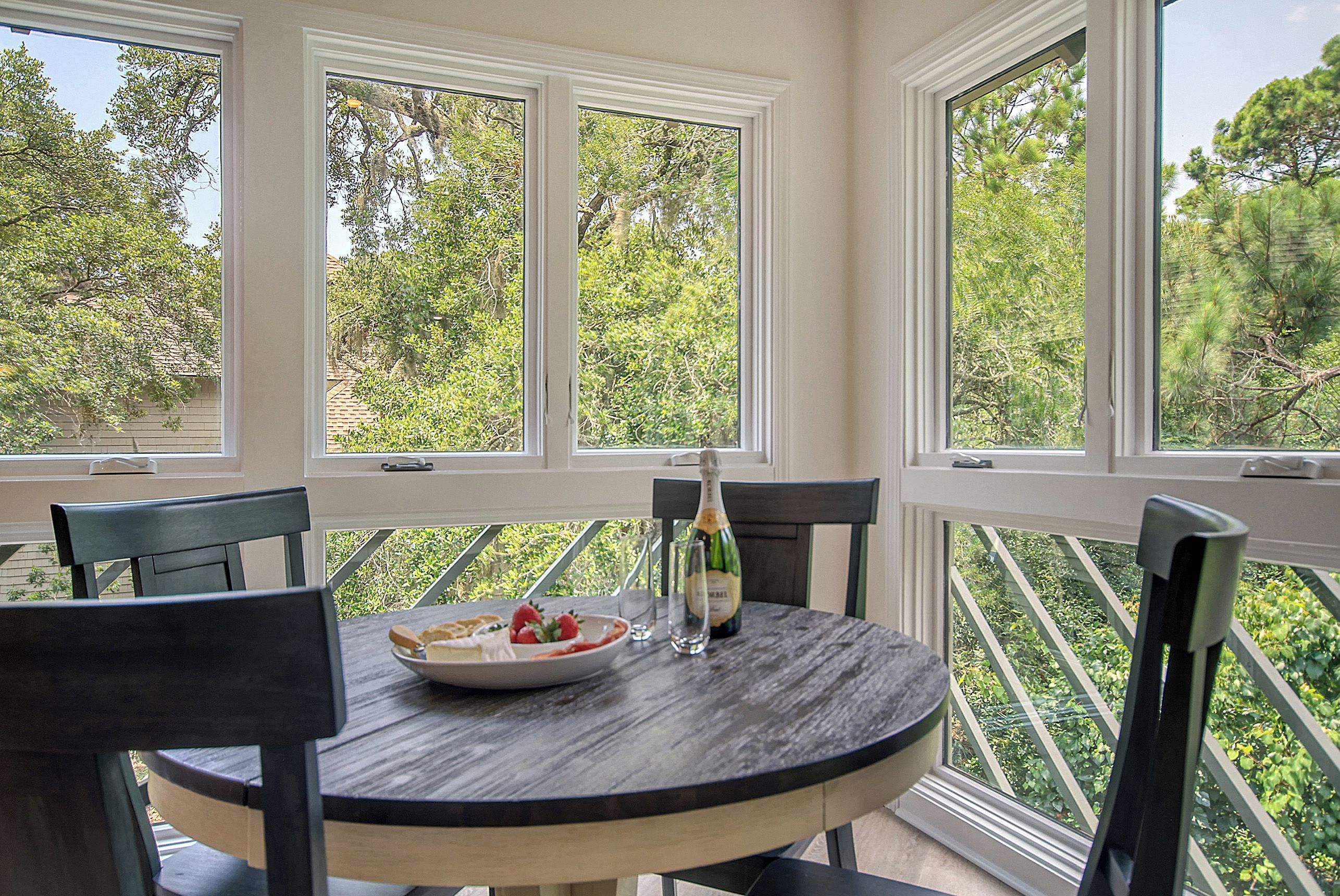 A round table with chairs, a bottle of champagne, and a plate of strawberries.