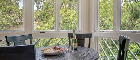 A round table with chairs, a bottle of champagne, and a plate of strawberries.