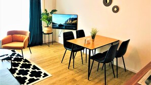 A modern living room with a wooden dining table, black chairs, a TV, and decorative wall art.