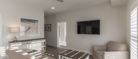 A spacious living room with a sofa, a coffee table, and a TV mounted on the wall.