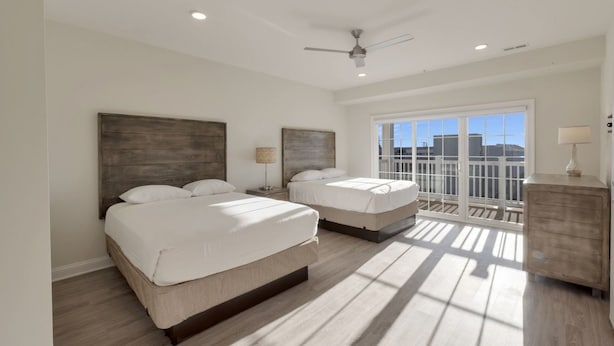 A bedroom with two beds, a ceiling fan, and a balcony with a view.