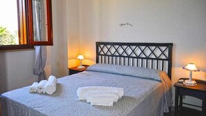 A neatly made bed with a headboard, two bedside lamps, and a window with curtains. - Holidaisy - Villa with garden (San Vito Lo Capo)
