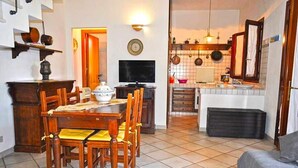 A dining area with a wooden table and chairs, a television, and a kitchen in the background. - Holidaisy - Villa with garden (San Vito Lo Capo)