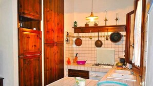 A kitchen with wooden cabinets, a tiled backsplash, hanging pots, a gas stove, and a double sink. - Holidaisy - Villa with garden (San Vito Lo Capo)