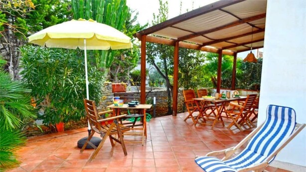 An outdoor patio with wooden furniture, a yellow umbrella, and a blue-striped lounge chair. - Holidaisy - Villa with garden (San Vito Lo Capo)