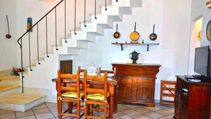 A dining area with a wooden table and chairs, a staircase with a railing, and a television on a wooden stand. - Holidaisy - Villa with garden (San Vito Lo Capo)