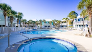 A swimming pool with a white fence, palm trees, and a row of colorful buildings in the background. - Seagrove 30A Beach Bungalow with Pool and Hot Tub (Santa Rosa Beach)