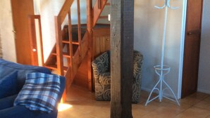 Ein Wohnzimmer mit einer Holztreppe, einem Sofa mit kariertem Kissen und einem Garderobenständer.